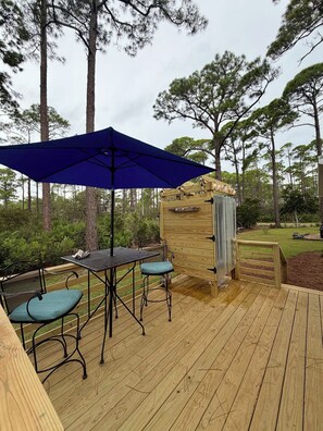 An outdoor deck with a table and chairs, a blue umbrella, and a wooden structure with a window.