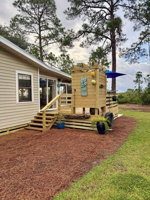 A wooden structure with a ramp leading to a door, surrounded by a mulched area and grass.