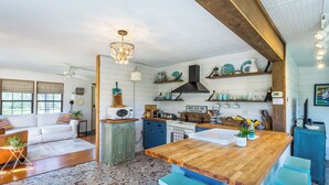 A kitchen with a wooden island, a stove, and a microwave. There are shelves above the stove and a sign that says "BEACH". - Marsh Beauty (Alligator Point)