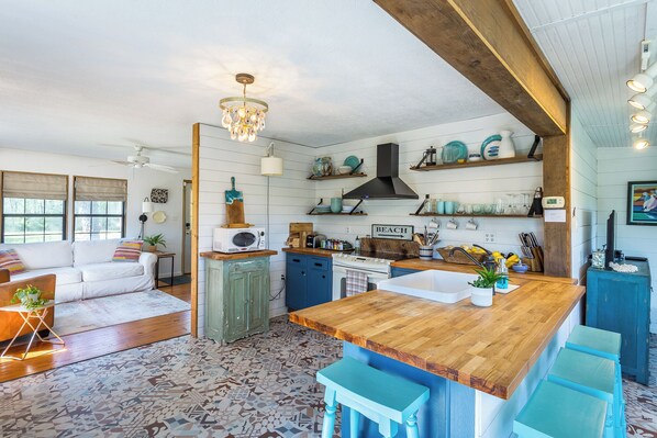 A kitchen with a wooden island, a stove, and a microwave. There are shelves above the stove and a sign that says "BEACH".