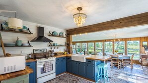 A kitchen with blue cabinets, a white stove, and a chandelier. - Marsh Beauty (Alligator Point)