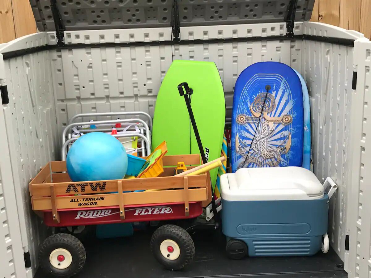 A storage unit with a blue cooler, a green paddleboard, a blue surfboard, and a wooden wagon labeled "ATW ALL-TERRAIN WAGON."