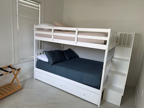 A bunk bed with a storage drawer, a wooden chair, and a radiator.