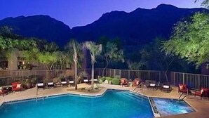 Ein Poolbereich mit Liegestühlen und Blick auf die Berge in der Abenddämmerung.