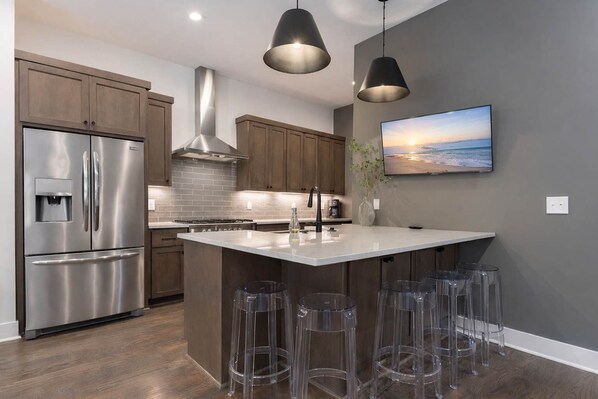 Una cocina moderna con electrodomésticos de acero inoxidable, una isla central con taburetes de bar y un televisor montado.