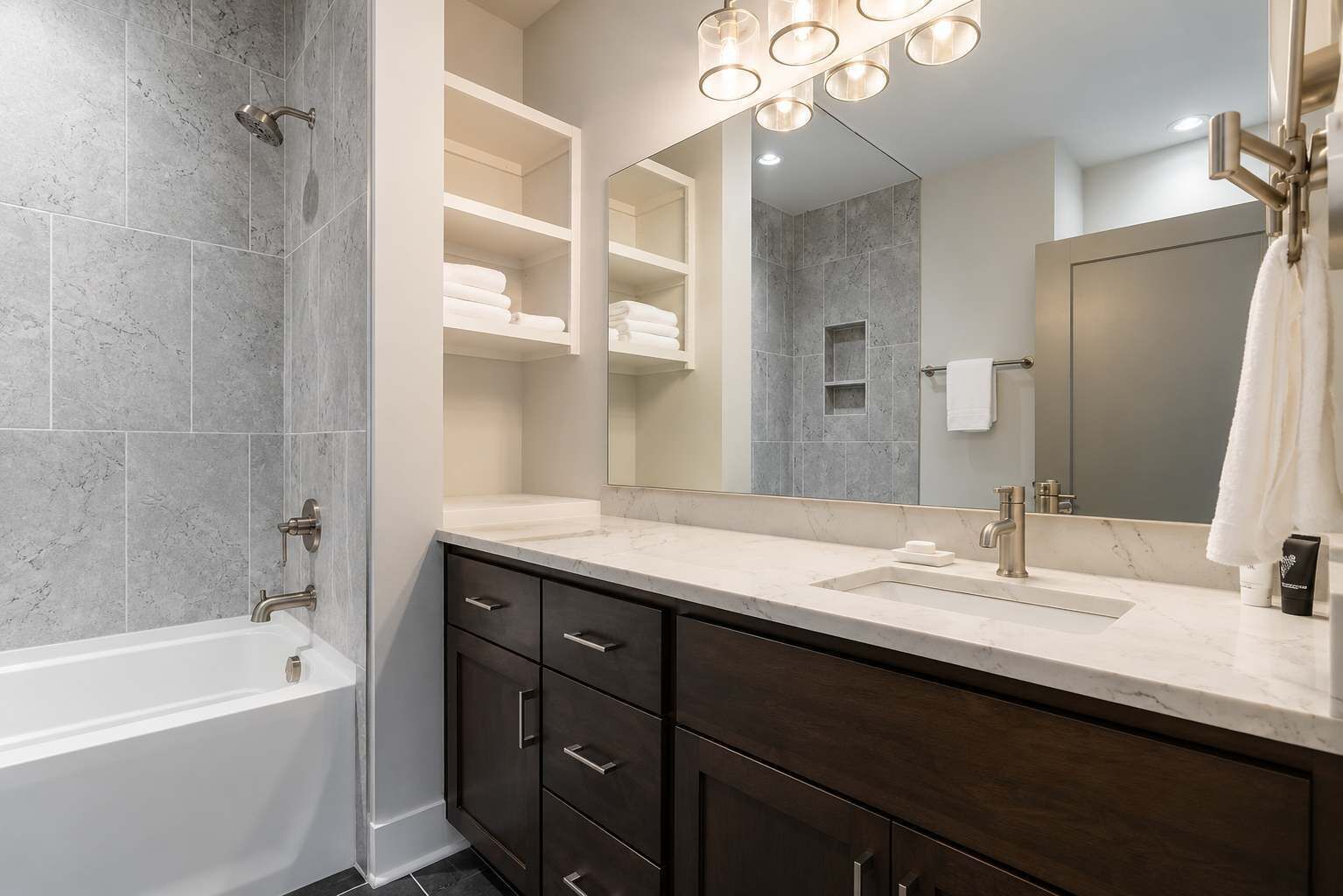 A modern bathroom with a bathtub, a vanity with a mirror, and built-in shelves for towels.