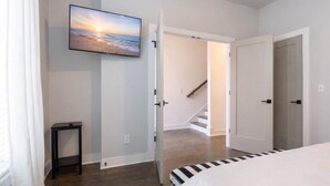 Un dormitori amb un llit, una televisió penjada a la paret, una escala i una porta que dona a una altra habitació.