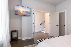 A bedroom with a bed, a TV mounted on the wall, a staircase, and a door leading to another room. - Cozy Nashville Home • Walk to Vandy (nashville)