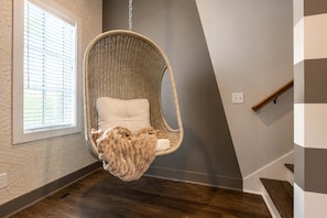 A hanging chair with a cushion and a blanket, a window with blinds, and a staircase with a wooden handrail. - Cozy Nashville Home • Walk to Vandy (nashville)
