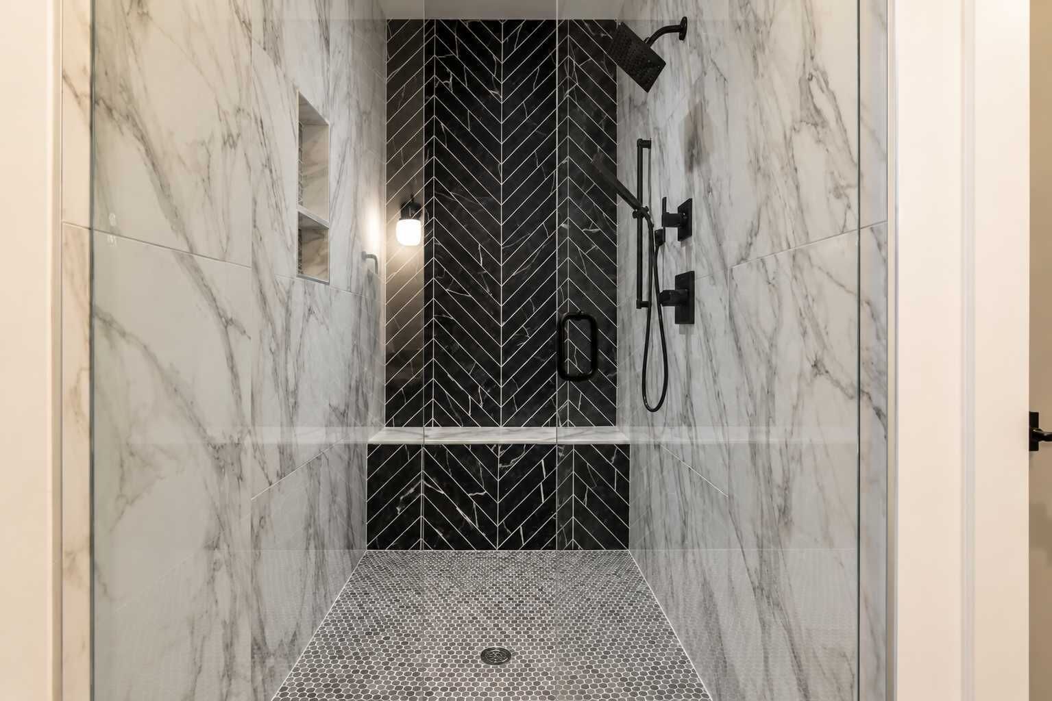 Un bagno doccia moderno con un motivo a spina di pesce sui muri e una porta in vetro.