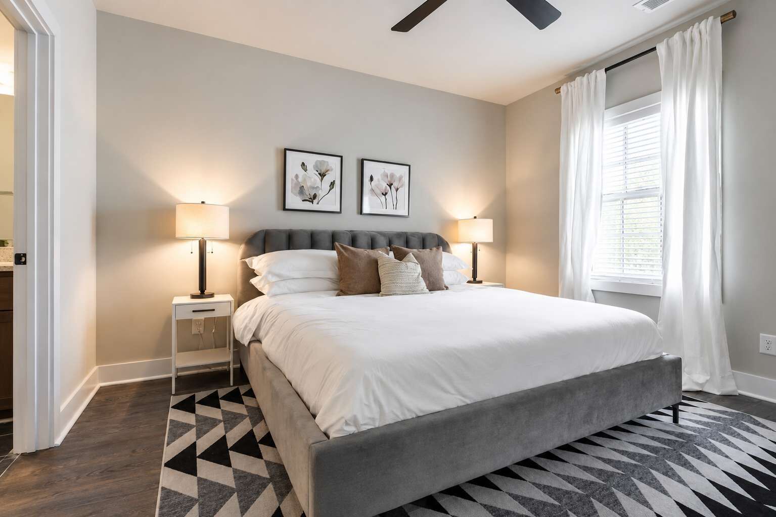 A modern bedroom with a large bed, two bedside lamps, and a ceiling fan.