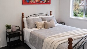 A bedroom with a bed, a ceiling fan, a window, a bedside table with a plant, and a painting on the wall. - Golfside Getaway by Ready Set Stay - Neat bungalow,WIFI,linen & towels included (Rosebud)