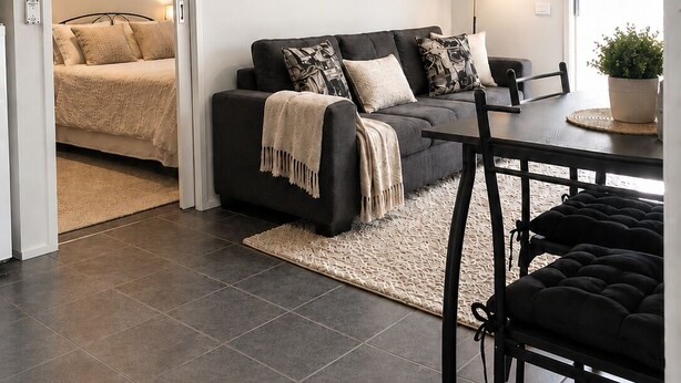 A modern living room with a sofa, a dining table, and a ceiling fan. - Golfside Getaway by Ready Set Stay - Neat bungalow,WIFI,linen & towels included (Rosebud)
