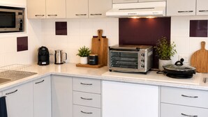 A modern kitchen with white cabinets, a built-in microwave, a toaster, and a coffee maker. - Golfside Getaway by Ready Set Stay - Neat bungalow,WIFI,linen & towels included (Rosebud)