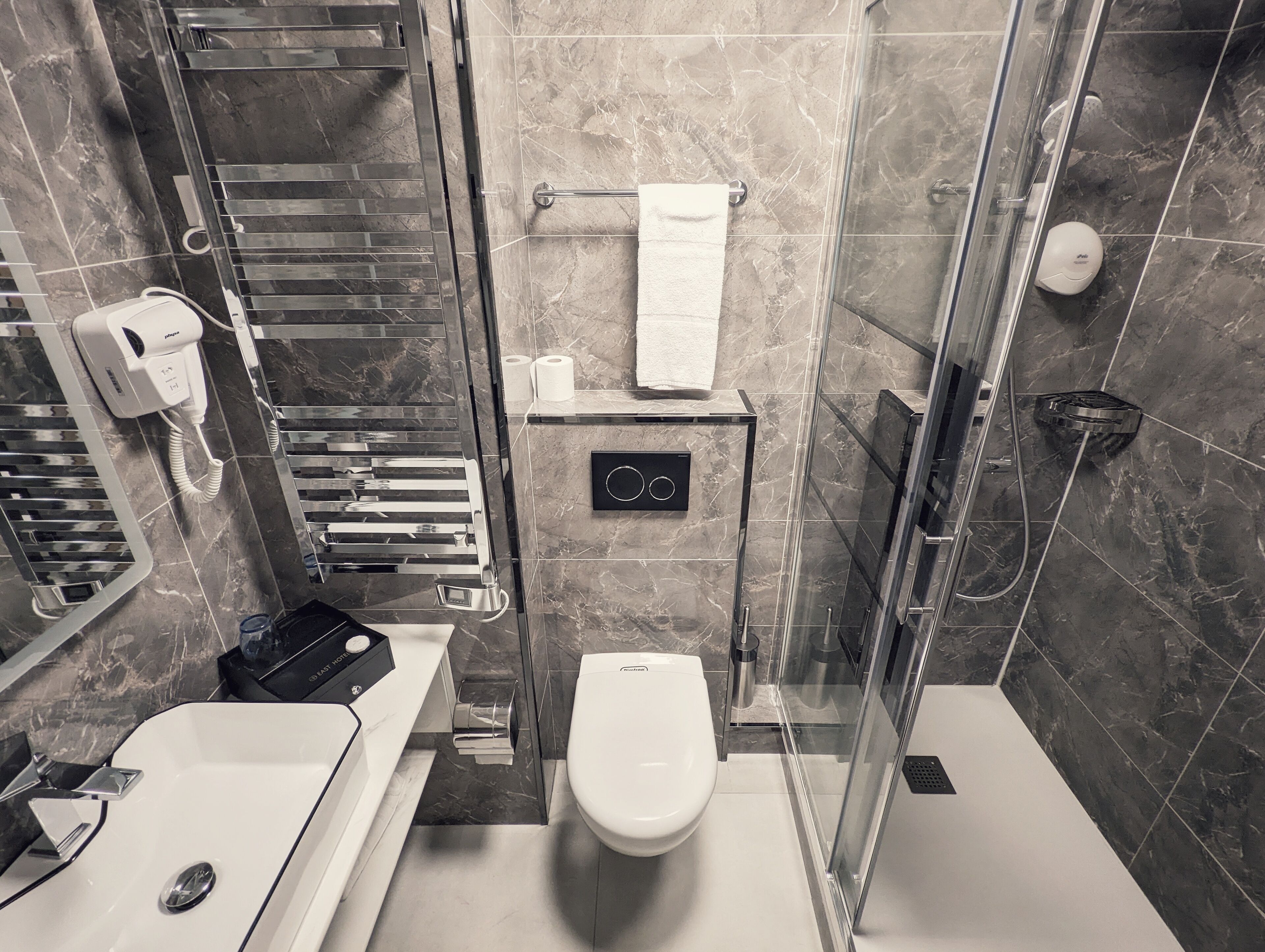 Un baño moderno con cabina de ducha de vidrio, inodoro, lavabo y perchero para toallas.