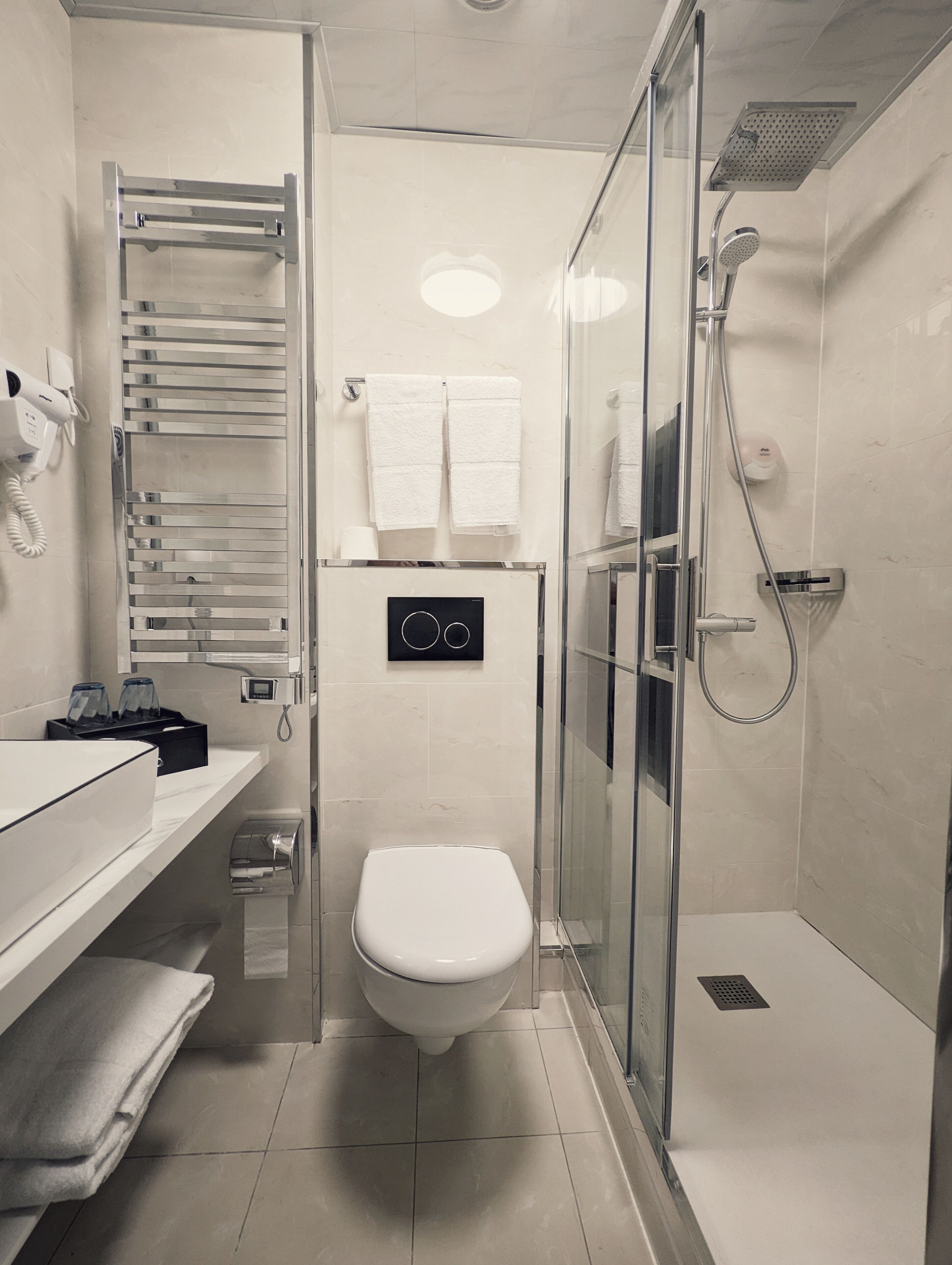 A modern bathroom with a glass-enclosed shower, a toilet, and a towel rack.