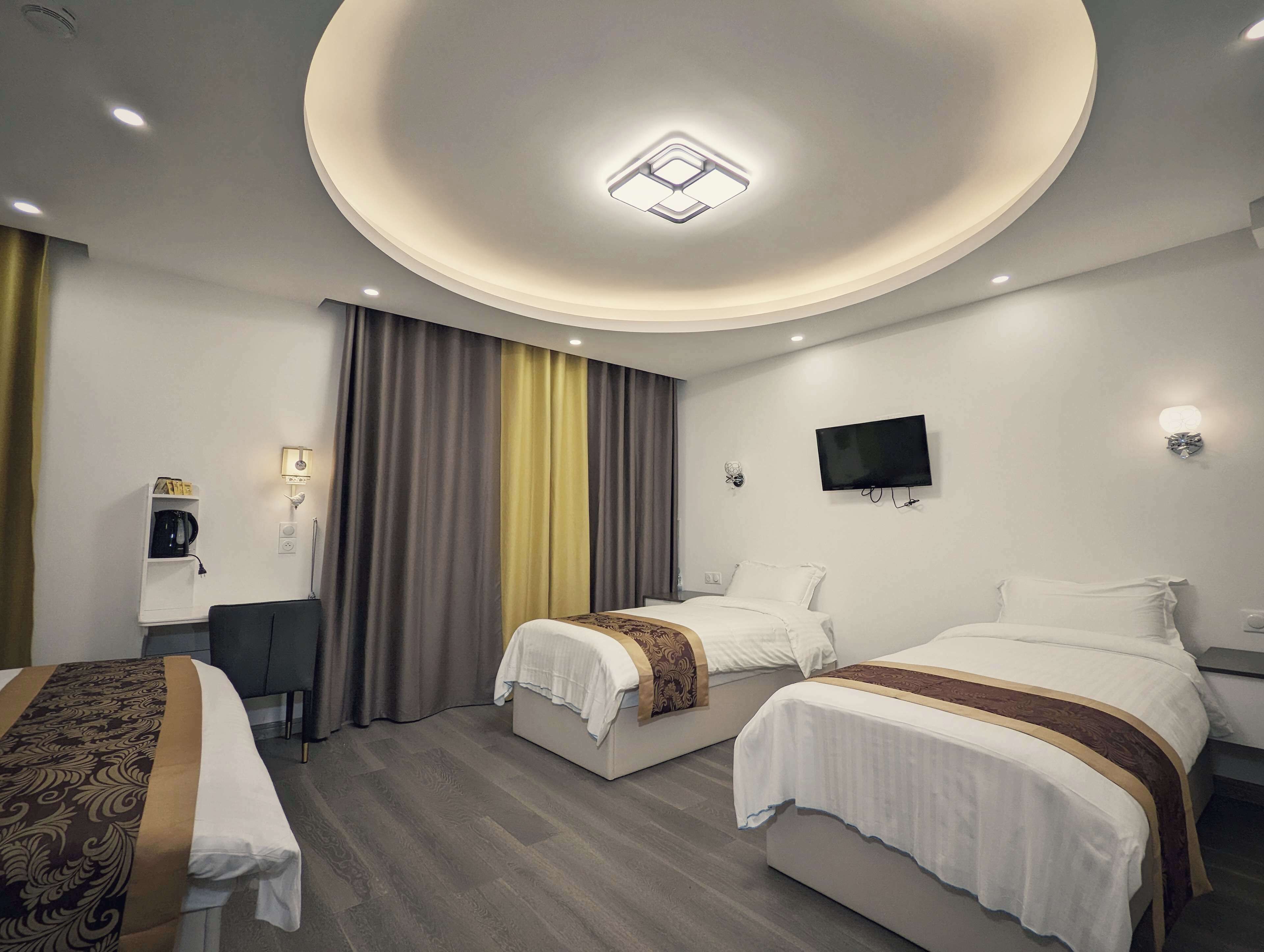 A hotel room with two beds, a desk, a television, and a ceiling light fixture.