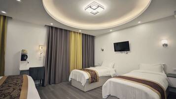 A hotel room with two beds, a desk, a television, and a ceiling light fixture.