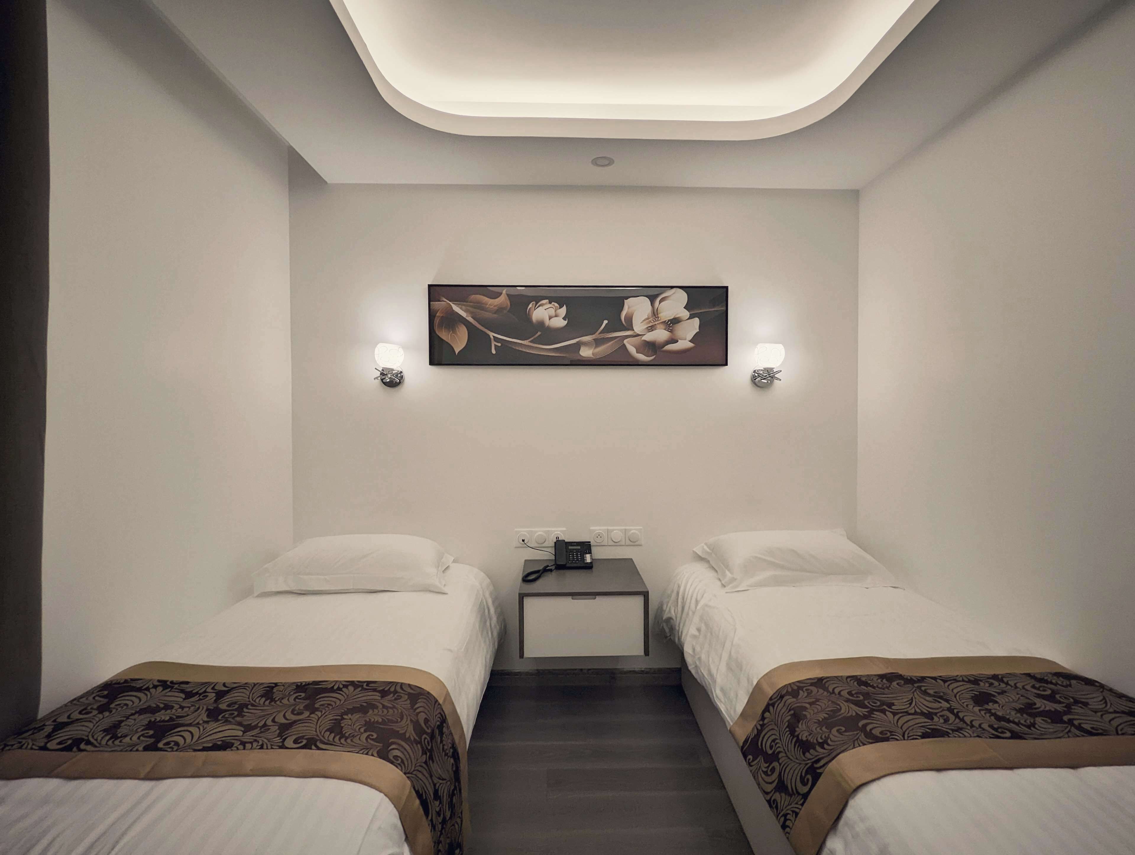 Quarto de hotel com duas camas, uma mesa de cabeceira, uma obra de arte na parede e iluminação embutida no teto.