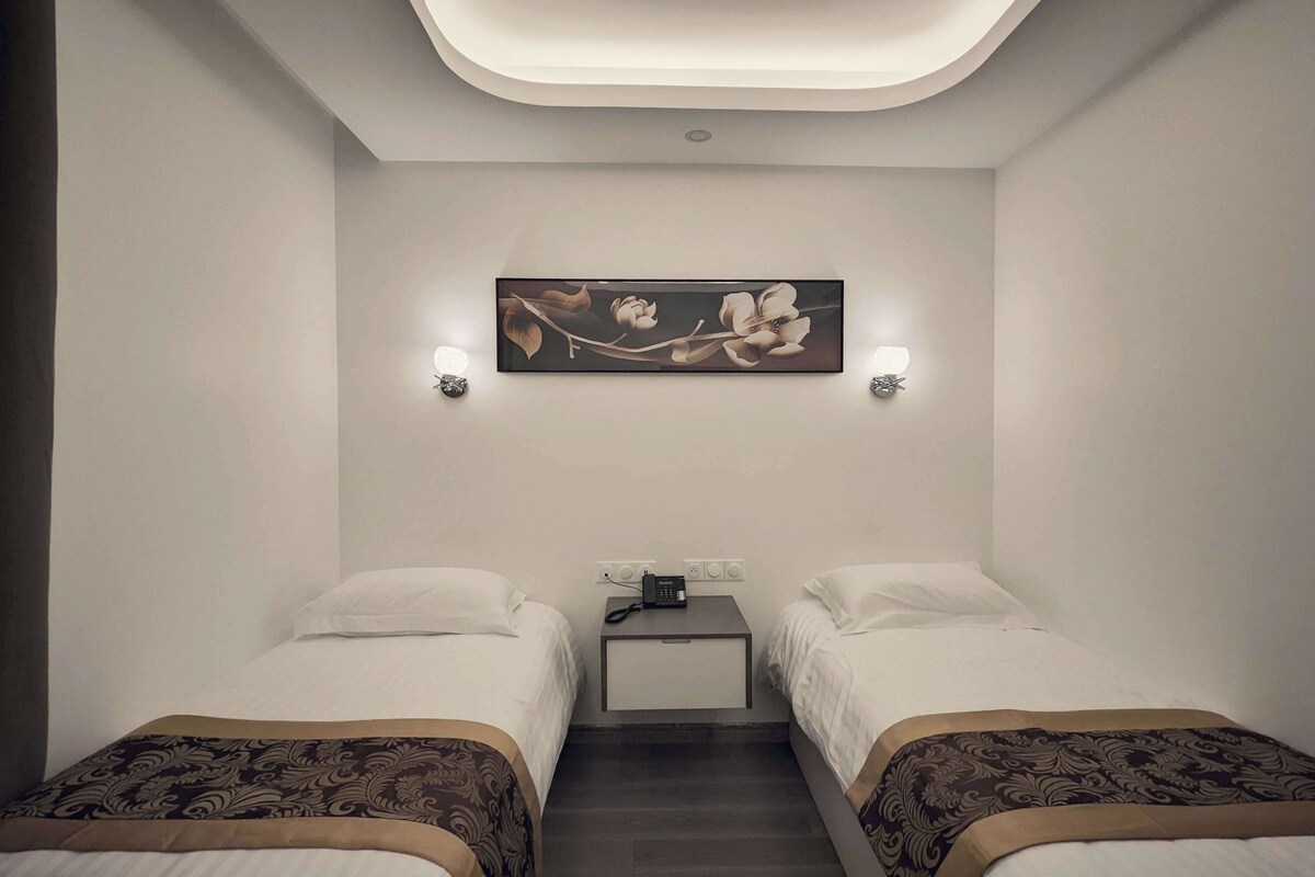 Une chambre d’hôtel avec deux lits, une table de chevet, une œuvre d’art accrochée au mur et des spots encastrés au plafond.