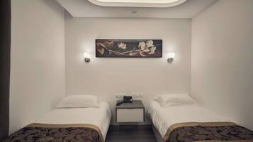 Quarto de hotel com duas camas, uma mesa de cabeceira, uma obra de arte na parede e iluminação embutida no teto.