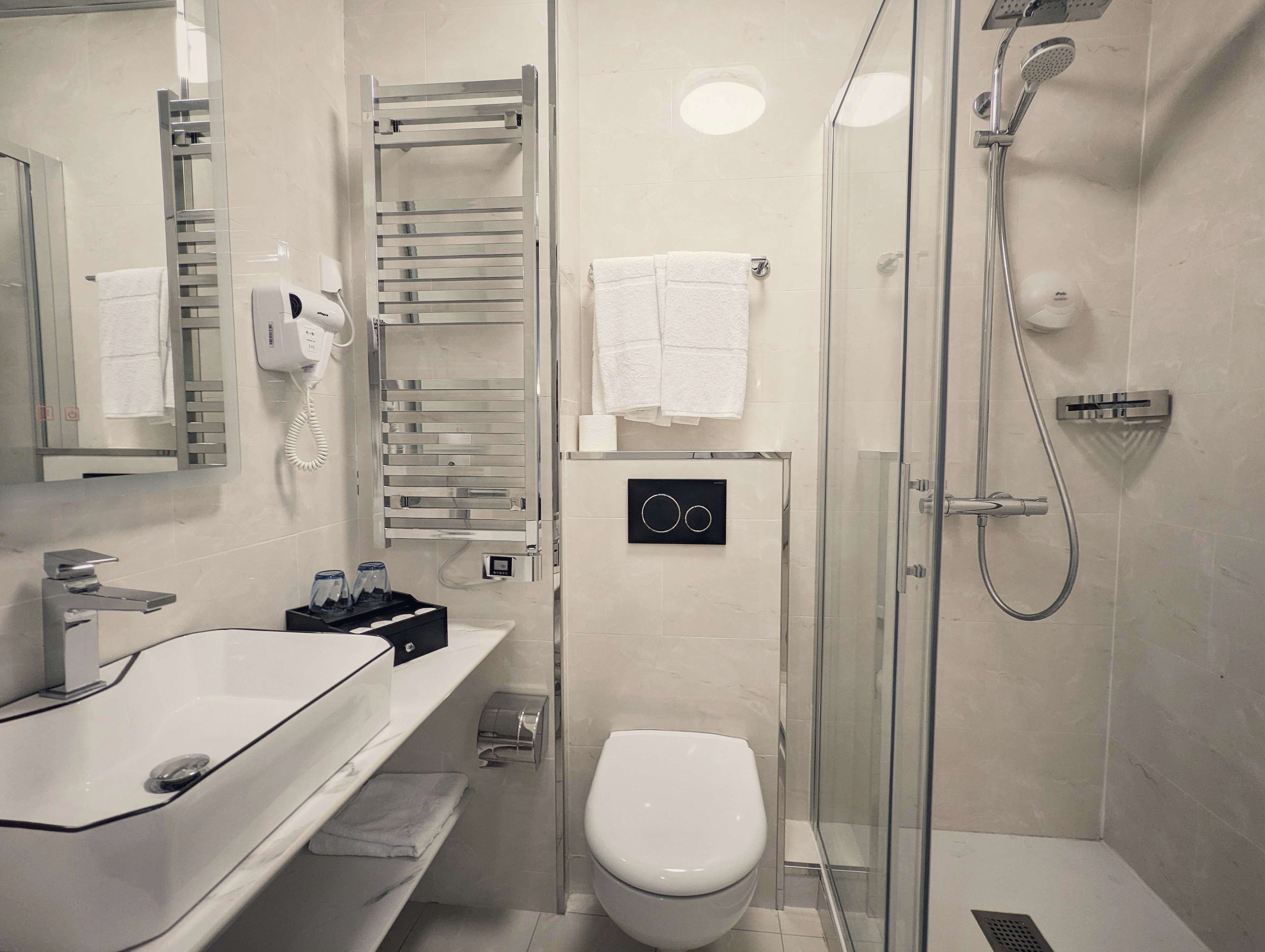 A modern bathroom with a glass-enclosed shower, a white toilet, and a sink with a towel rack.