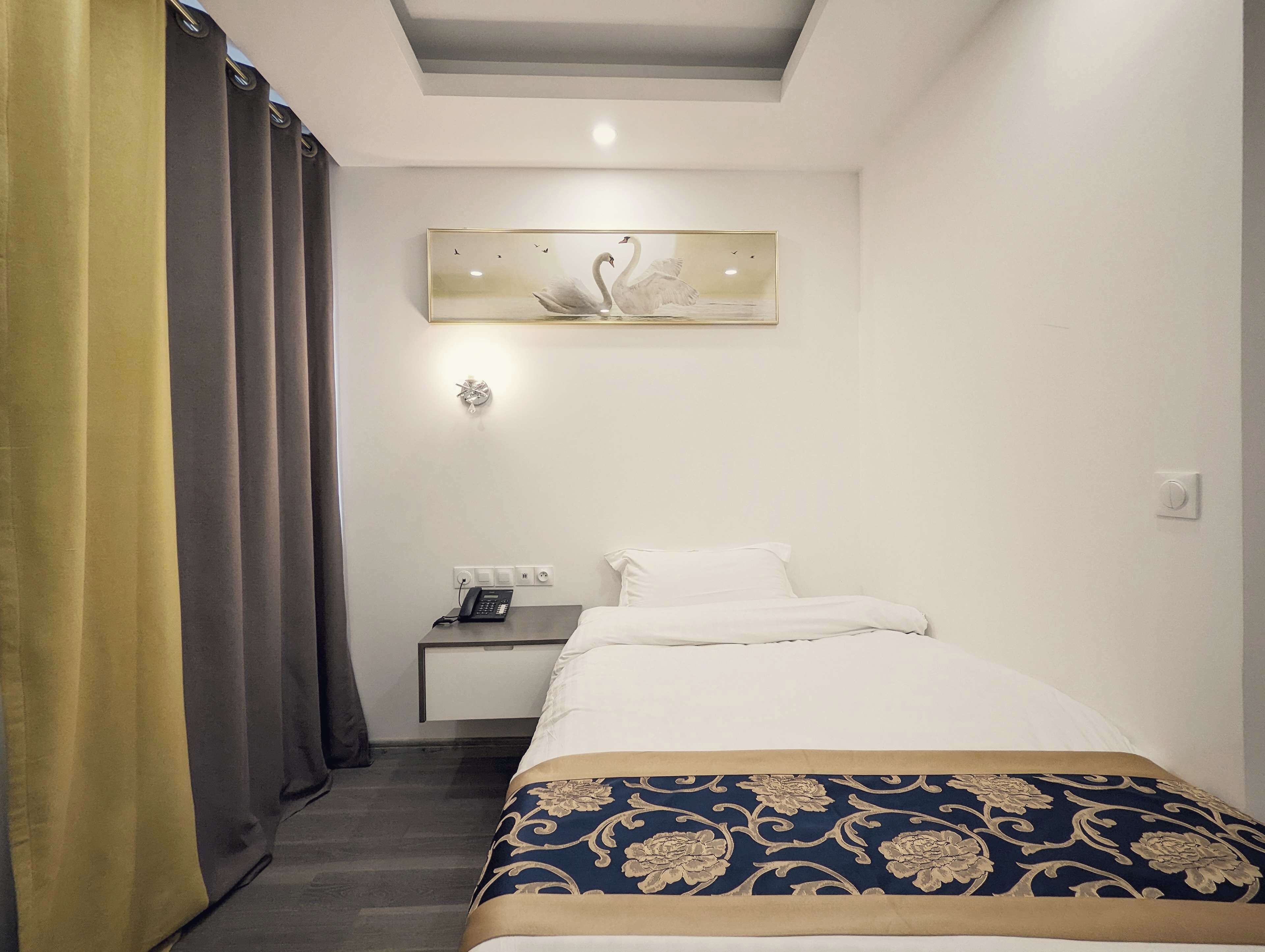 A hotel room with a bed, a bedside table, a lamp, and a painting of swans on the wall.