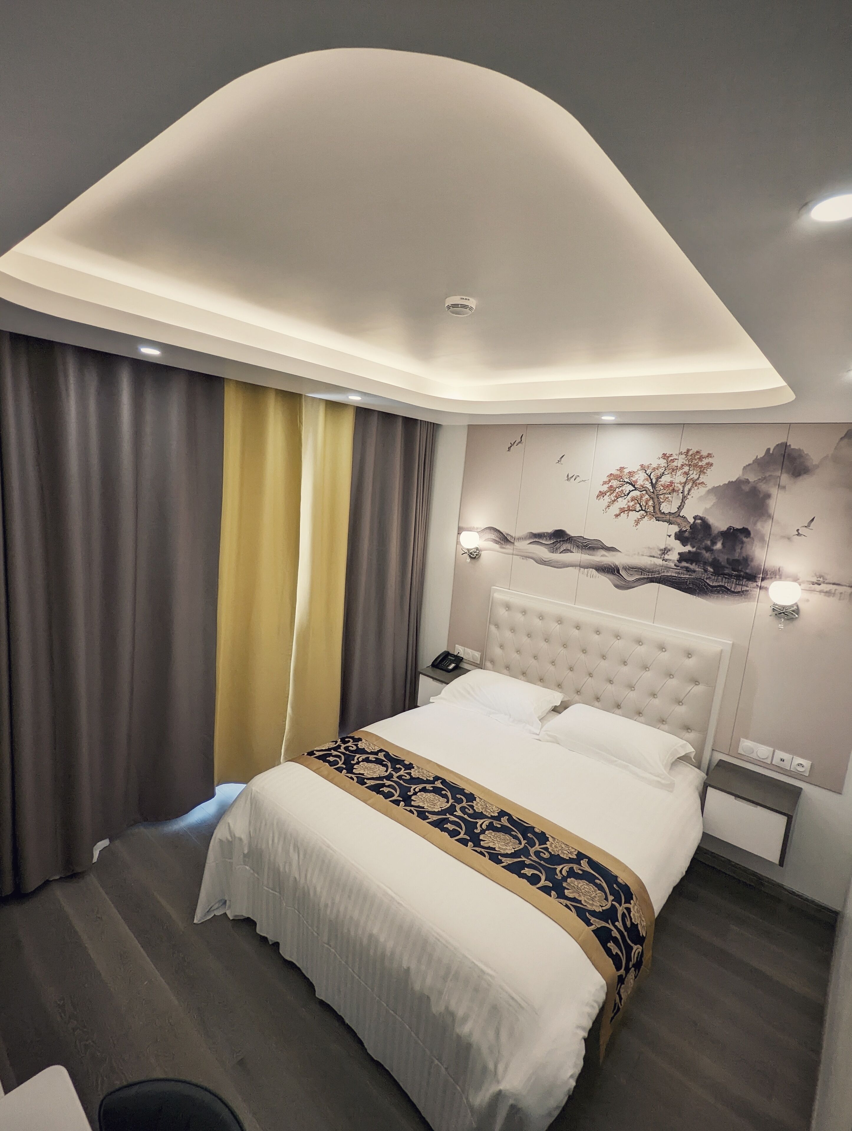 Una habitación de hotel moderna con una cama grande, un cabecero capitonado, un teléfono montado en la pared y un cuadro decorativo.
