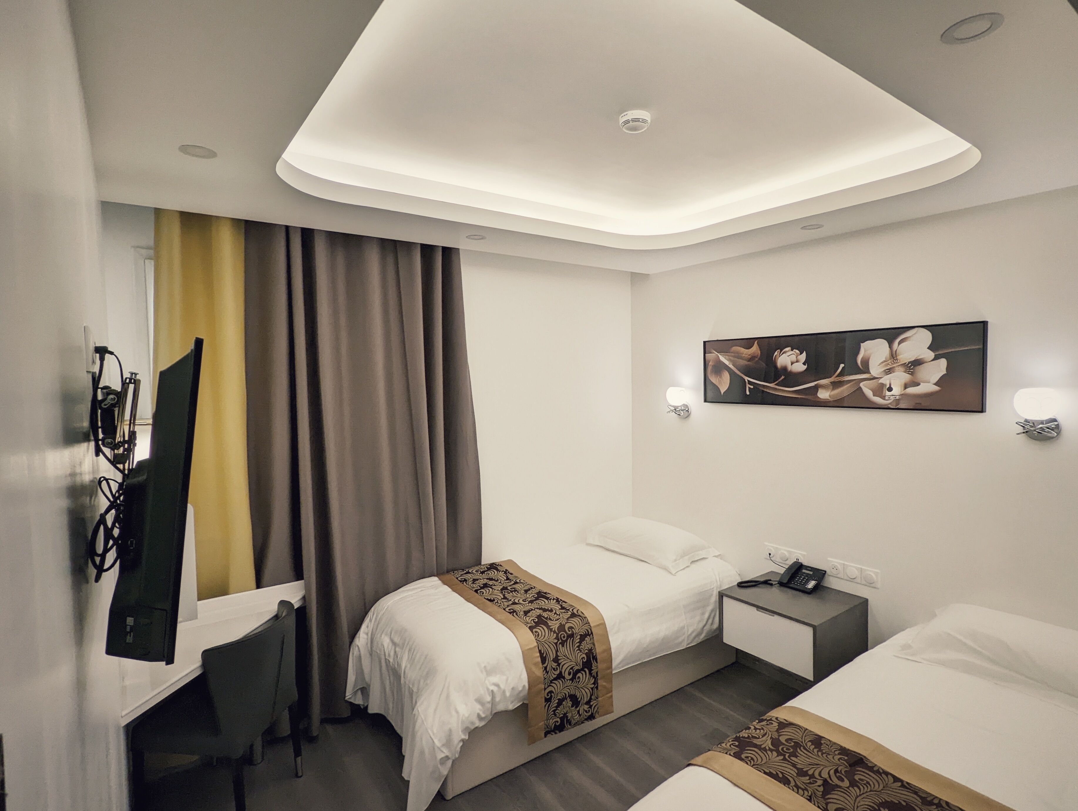 A hotel room with two beds, a desk, a chair, a desk lamp, a telephone, and a painting on the wall.