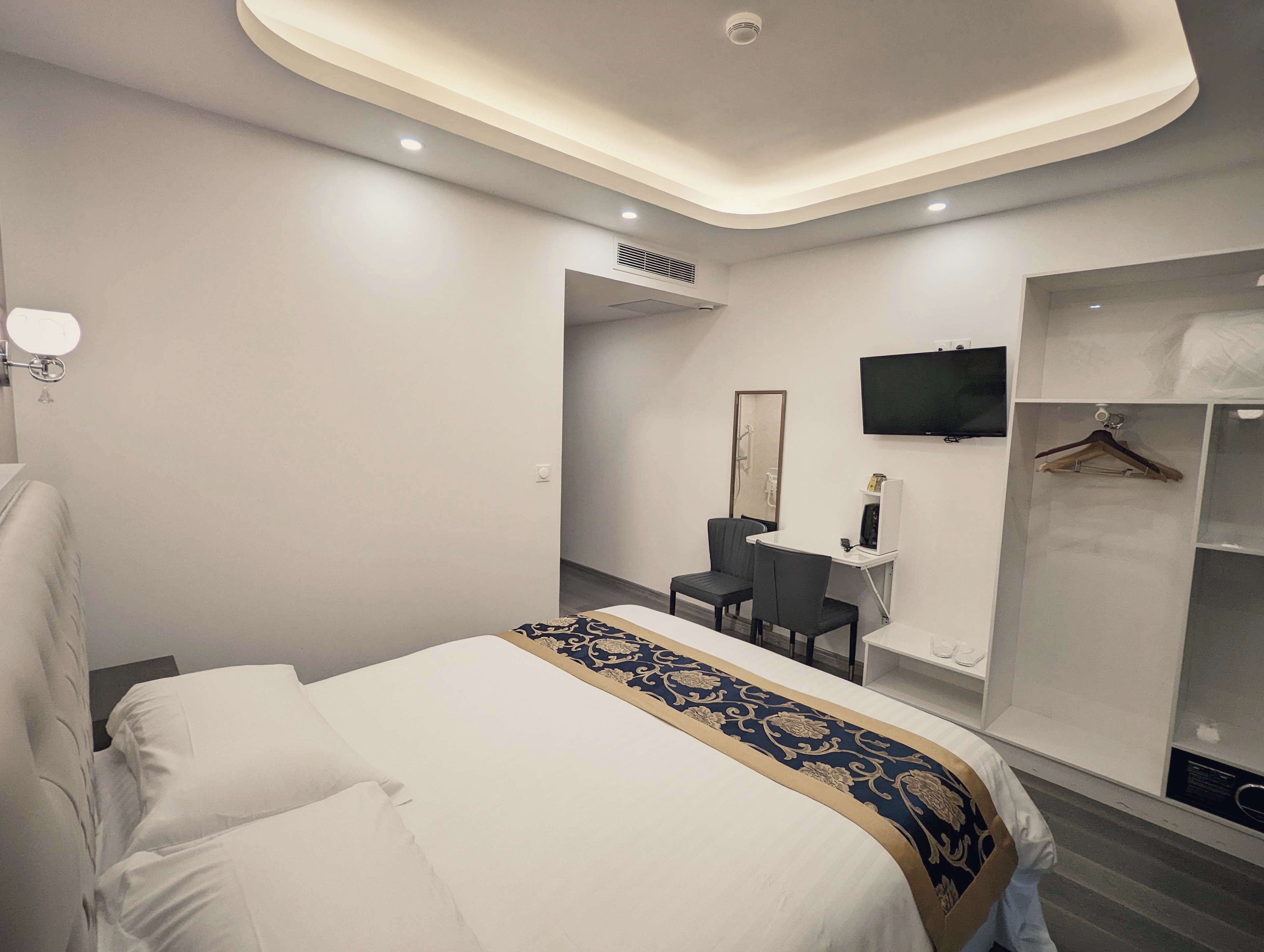 Una habitación de hotel moderna con una cama bien hecha, un escritorio con una silla, un televisor y un armario.