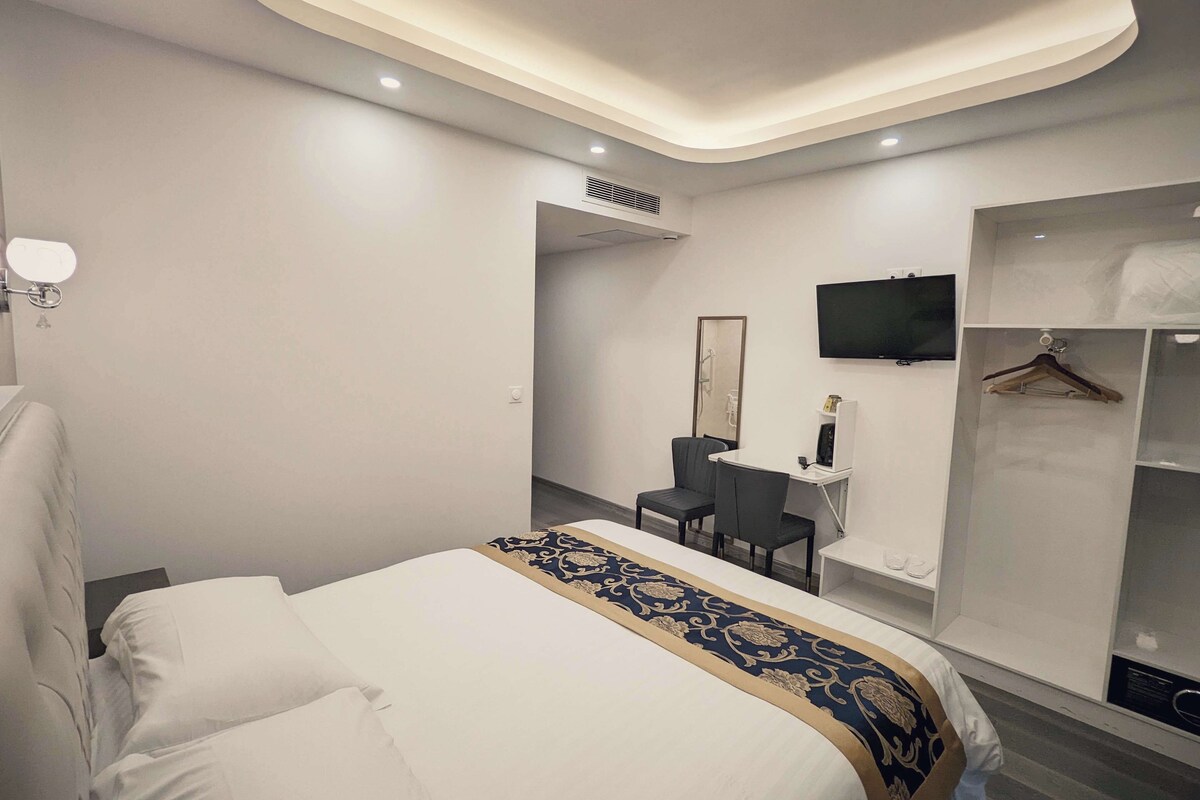 Une chambre d’hôtel moderne avec un lit bien fait, un bureau avec une chaise, une télévision et une armoire.