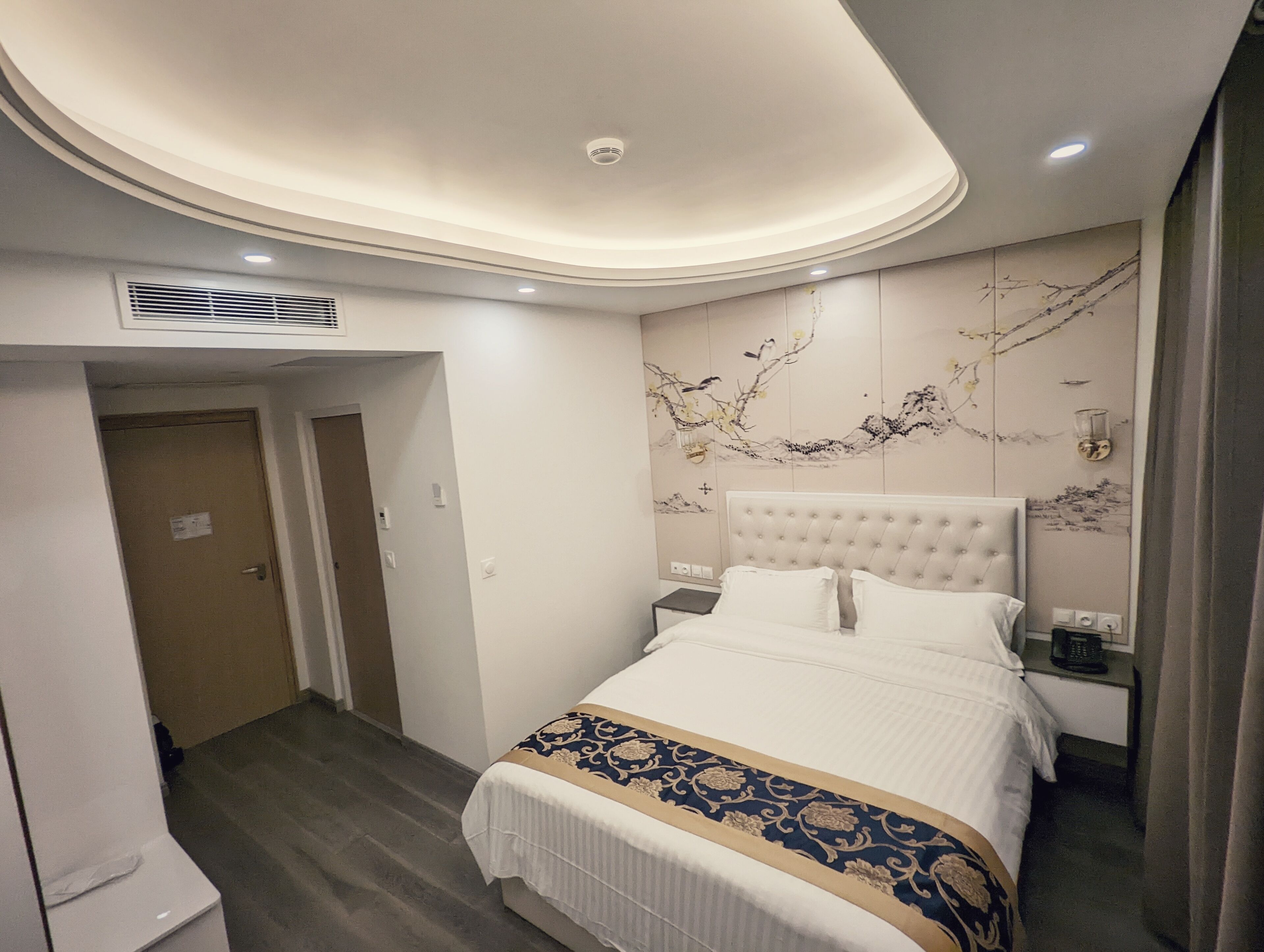 Ein Hotelzimmer mit einem großen Bett, einem Nachttisch, einer Wandlampe und einer Deckenleuchte.