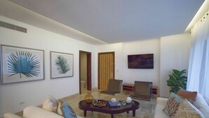 Una sala de estar con sofá, mesa de centro y sillas, con obras de arte en las paredes y un televisor colgado.
