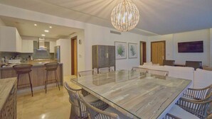 Una cocina moderna con una isla grande, taburetes de bar y una mesa de comedor de vidrio rodeada de sillas.