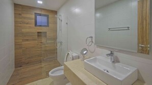 Un baño moderno con un panel de pared de madera, cabina de ducha de vidrio, inodoro, lavabo con espejo y un perchero para toallas.