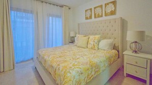 Un dormitorio con una cama grande, una mesita de noche y un ventanal con cortinas. Hay tres adornos colgados en la pared sobre la cama.