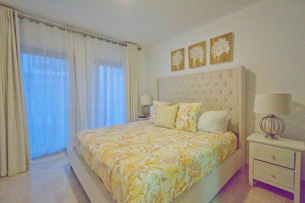 A bedroom with a large bed, a nightstand, and a window with curtains. There are three wall-mounted decorations above the bed.