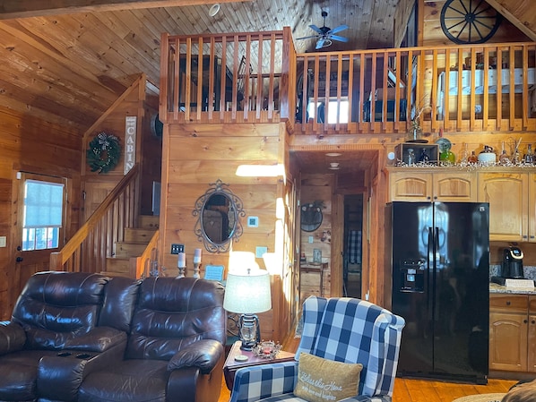 Cozy cabin interior with a leather sofa, checkered armchair, and wooden staircase.