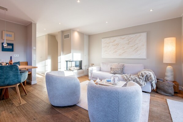 A modern living room with a white sofa, two grey poufs, a coffee table, and a fireplace.