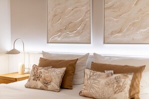 A bedroom with a bed, pillows, a nightstand, a lamp, and two abstract wall art pieces.