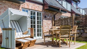 Une terrasse avec une table et des chaises en bois, un fauteuil de jardin à rayures et un espace salon abrité.