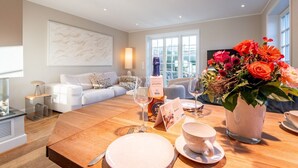 Un salon moderne avec une table à manger en bois, mise pour un repas, un canapé et une grande fenêtre laissant entrer la lumière naturelle.