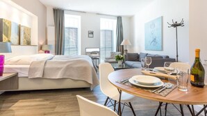 Una habitación de hotel moderna con una cama, una mesa de comedor para dos personas, un sofá y un televisor.