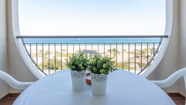 Varanda com vista clara para a praia e o oceano. Há duas plantas em vasos sobre a mesa.