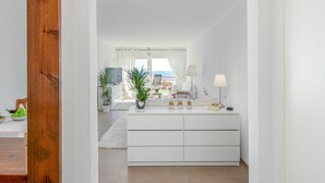 Quarto de hotel moderno com penteadeira branca, televisão e vista para o mar.