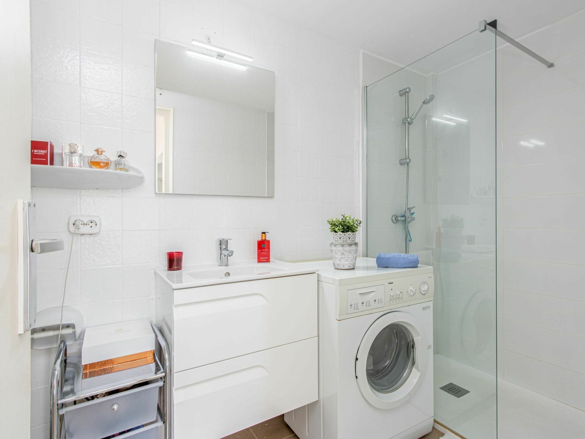 A modern bathroom with a glass shower enclosure, a built-in washing machine, and a mirror above the sink.