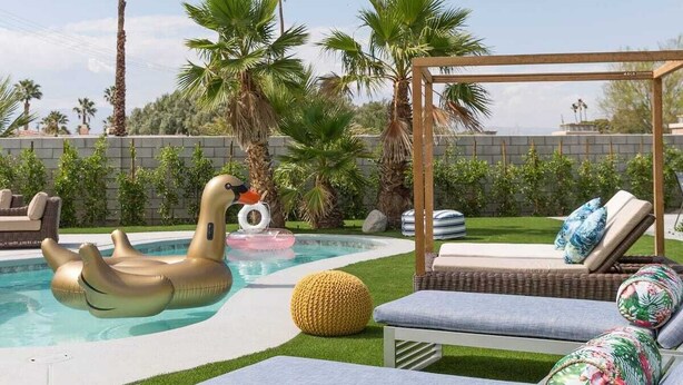 Un área de piscina con un juguete flotante, césped artificial y sillones de jardín con cojines.