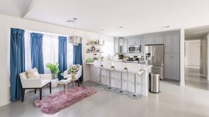 Una cocina moderna con gabinetes grises, electrodomésticos de acero inoxidable y una zona de bar con taburetes blancos.