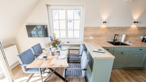 Een moderne keuken met een eetgedeelte, met een houten tafel, grijze gestoffeerde stoelen, een ingebouwd eiland met een spoelbak en een groot raam dat voor natuurlijk licht zorgt.