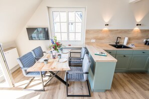 A modern kitchen with a dining area, featuring a wooden table, grey upholstered chairs, a built-in island with a sink, and a large window providing natural light.
